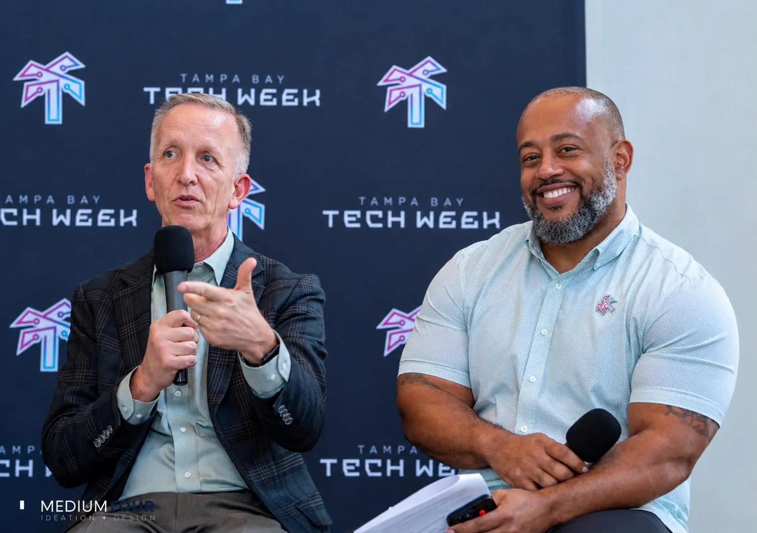 Michael Hall and Jesus Vidaurri speaking on stage in front of a Tampa Bay Tech Week backdrop